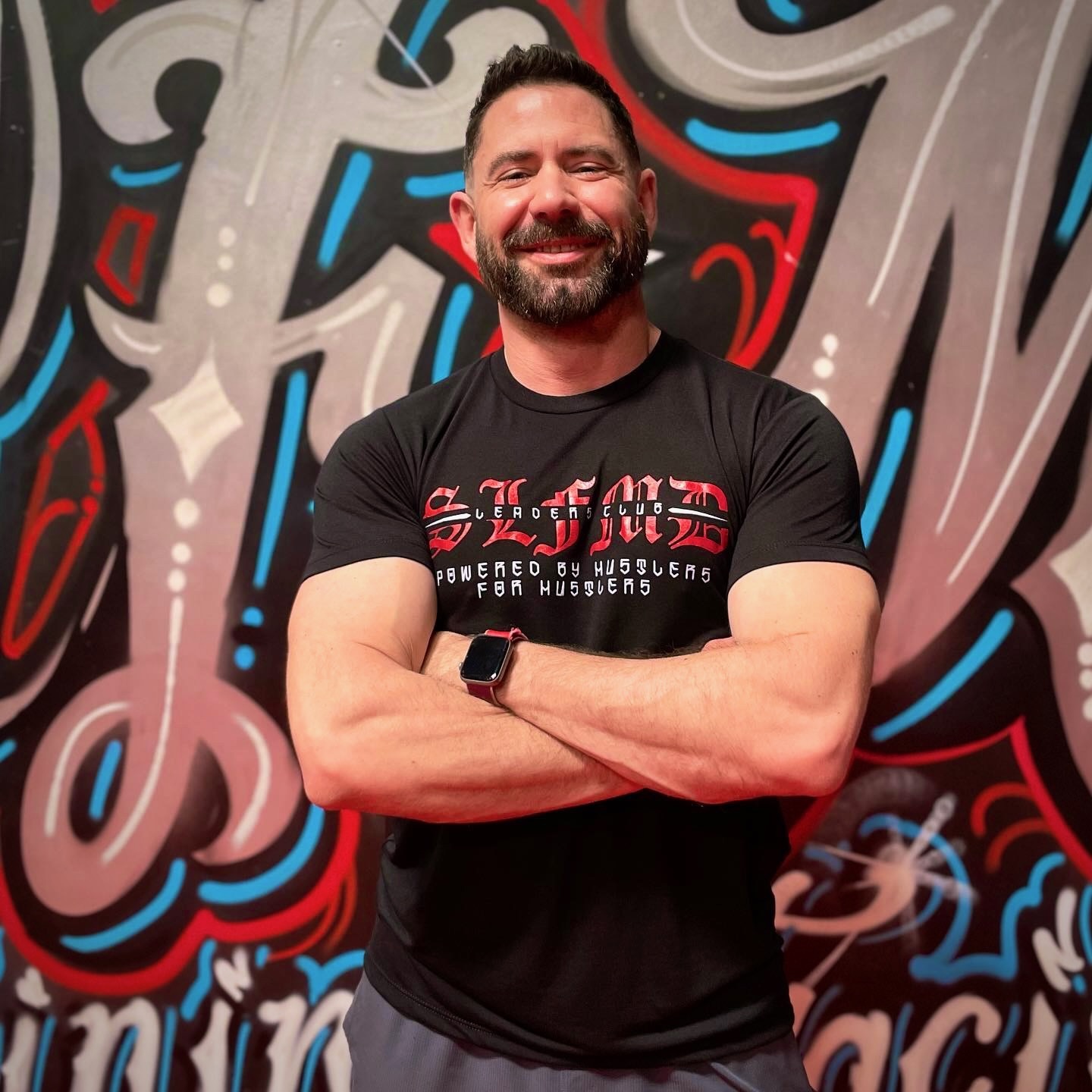 Coach Chris standing with his arms crossed in front of the gym's graffiti mural