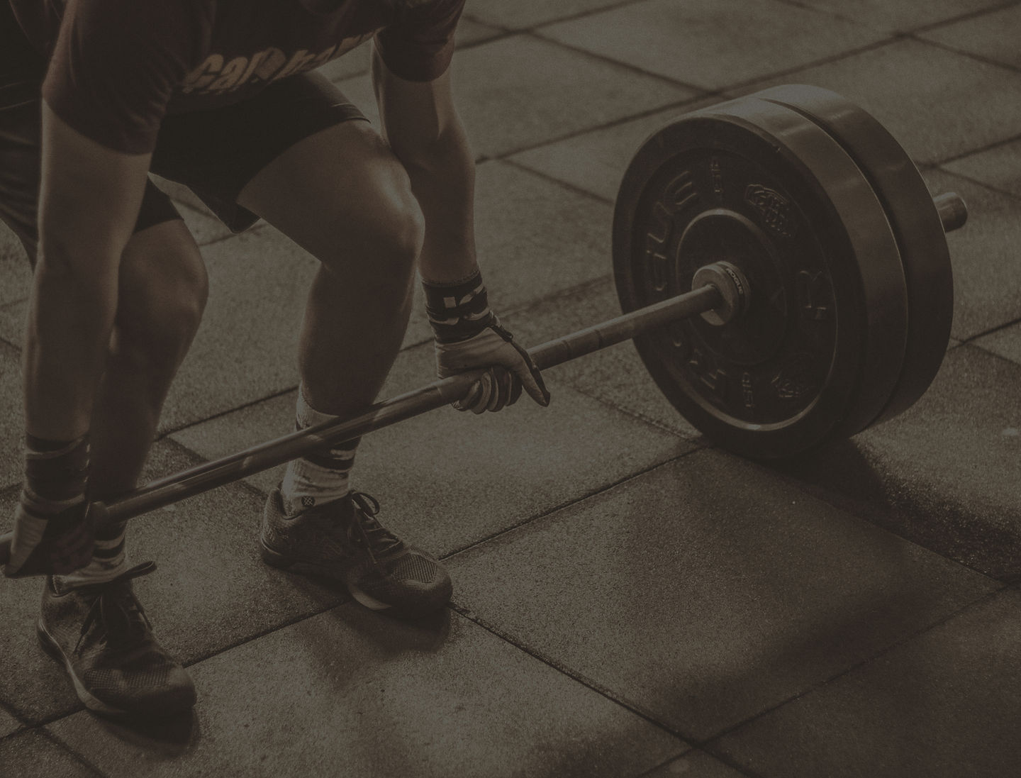 A lifter gripping a loaded barbell at the bottom of a deadlift setup