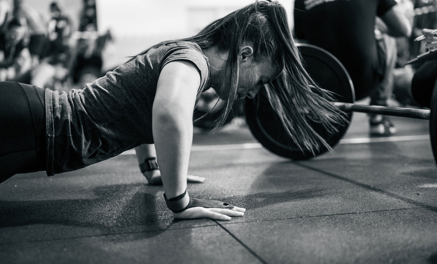 A client at the bottom of a pushup with a loaded barbell on the floor beside her