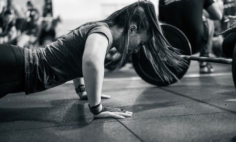 A client at the bottom of a pushup beside a loaded barbell on the gym floor