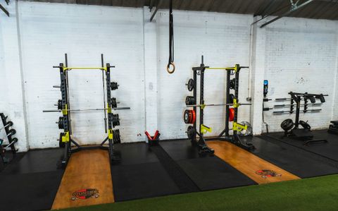 Placeholder photograph: two loaded power racks against a white brick wall, wooden lifting platforms in front of them and a lane of turf across the foreground